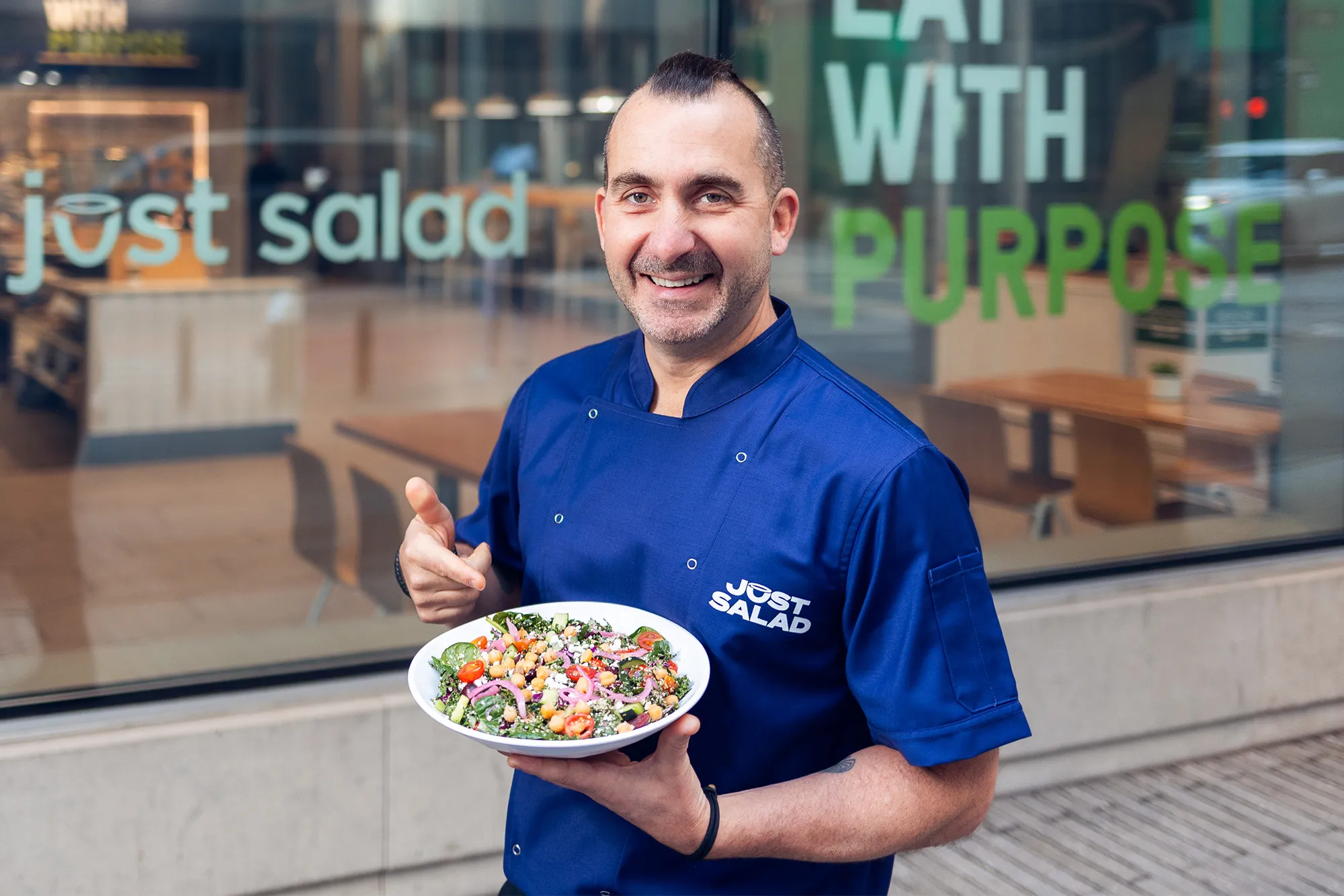 Chef Marc Forgione holding a salad in front of a Just Salad location